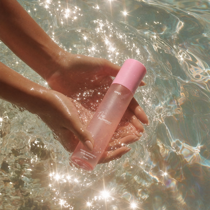 Mains tenant le flacon The Bloomist dans une eau scintillante