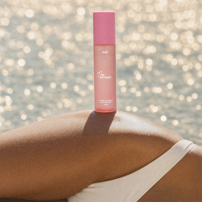 Flacon The Bloomist posé en équilibre sur la jambe d'une femme face à la mer