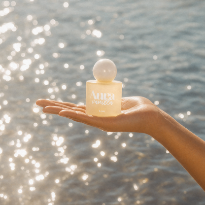 Flacon Aura Vanilla posé dans la paume d'une main devant la mer
