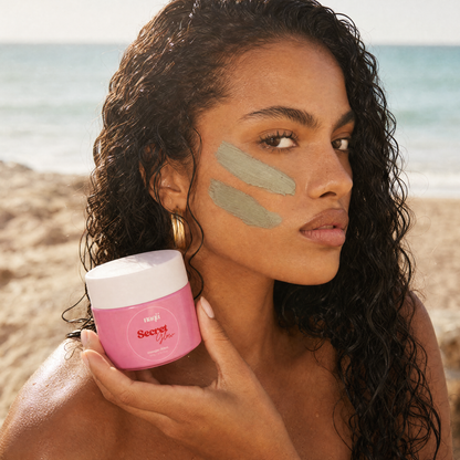 Femme à la plage, deux traits de masque Secret Glow sur la joue, pot naqä en main
