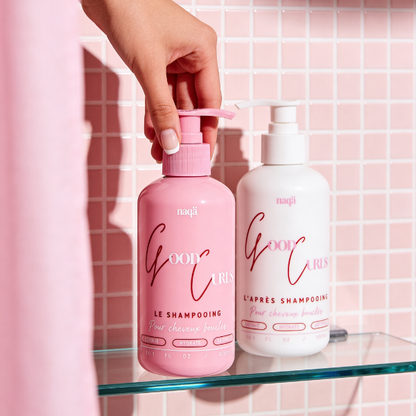 Duo Good Curls : main attrapant le shampooing rose à côté de l'après-shampooing blanc sur une étagère en verre